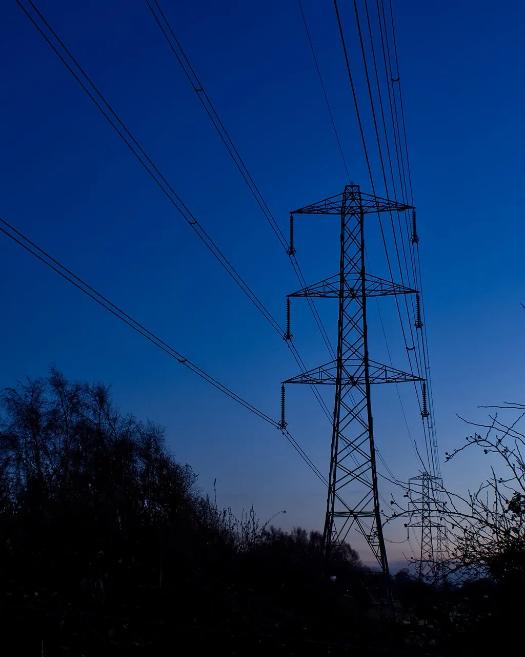 Electricity pylons and power lines against a deep blue sky after dusk in Cheshire.